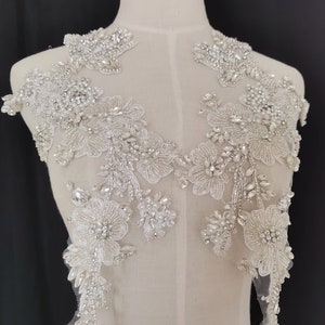 May include: A delicate white lace applique featuring intricate floral designs and sparkling rhinestones. The applique is ideal for adding a touch of elegance to wedding dresses, bridal accessories, or other special occasion garments.