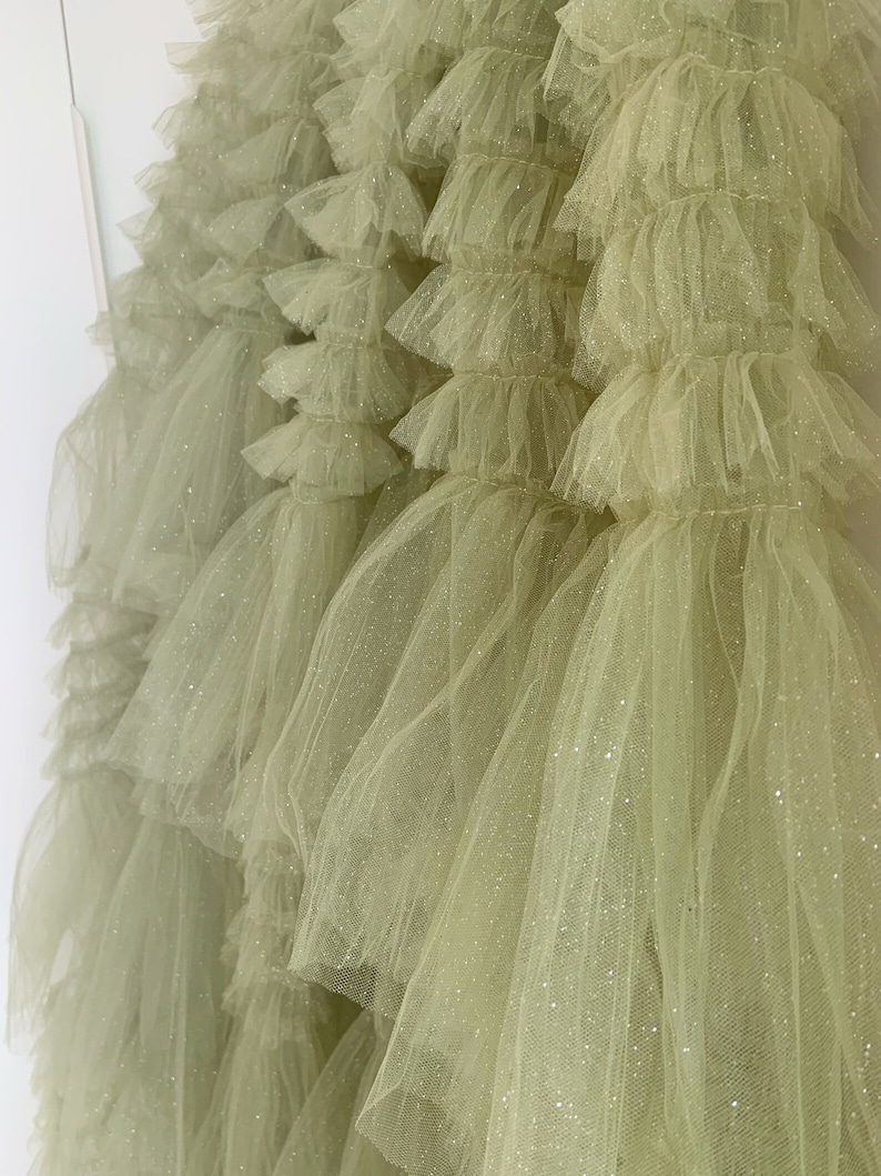 May include: A light green tulle fabric with a sparkly finish. The fabric is layered and ruffled, creating a voluminous and textured look.