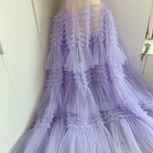 May include: A lavender tulle dress with multiple layers of ruffles. The dress is sheer and has a flowing silhouette.