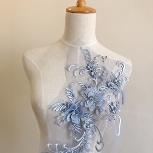 May include: A light blue floral applique with pearl and rhinestone embellishments. The applique is on a sheer mesh fabric and is ideal for adding a touch of elegance to any garment.