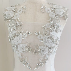 May include: A pair of white lace appliques with silver rhinestone embellishments. The appliques are designed with floral motifs and are perfect for adding a touch of sparkle to a wedding dress or other special occasion garment.