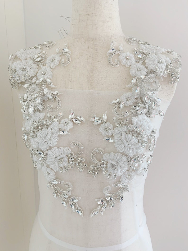 May include: A pair of white lace appliques with silver rhinestone embellishments. The appliques are designed with floral motifs and are perfect for adding a touch of sparkle to a wedding dress or other special occasion garment.
