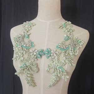 Puede incluir: Un par de apliques de cuentas verde claro y plateadas. Los apliques presentan un diseño floral con pedrería transparente y cuentas verde claro. Los apliques se exhiben en un maniquí. El fondo es negro.