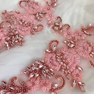 May include: Two pink floral appliques with rhinestones and beads. The appliques are on a white background.