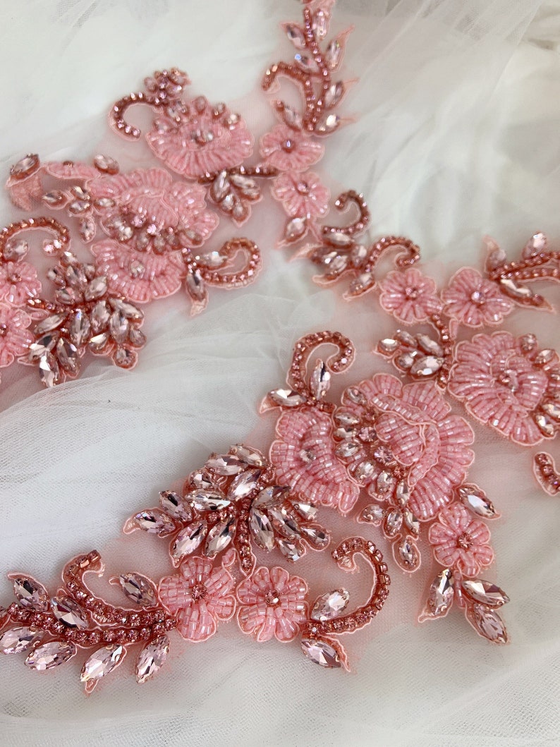May include: Two pink floral appliques with rhinestones and beads. The appliques are on a white background.