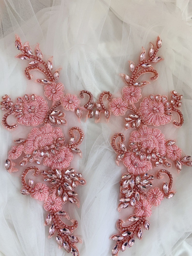 May include: Two delicate pink floral appliques with crystal embellishments. The appliques feature intricate floral designs with beaded flowers and sparkling crystals.