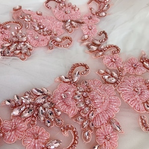 May include: Pink and rose gold beaded floral applique with rhinestones. This delicate embellishment features a floral design with intricate beading and sparkling rhinestones.