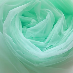 May include: A close-up of soft, mint green tulle fabric, gathered and draped in a delicate, flowing pattern.