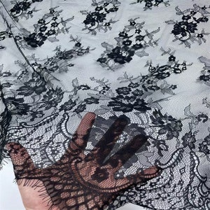 May include: Black lace fabric with a delicate floral pattern. The lace has a scalloped edge and is sheer.