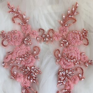 May include: Two pink beaded floral appliques with crystal embellishments. The appliques are perfect for adding a touch of elegance to any garment or craft project.