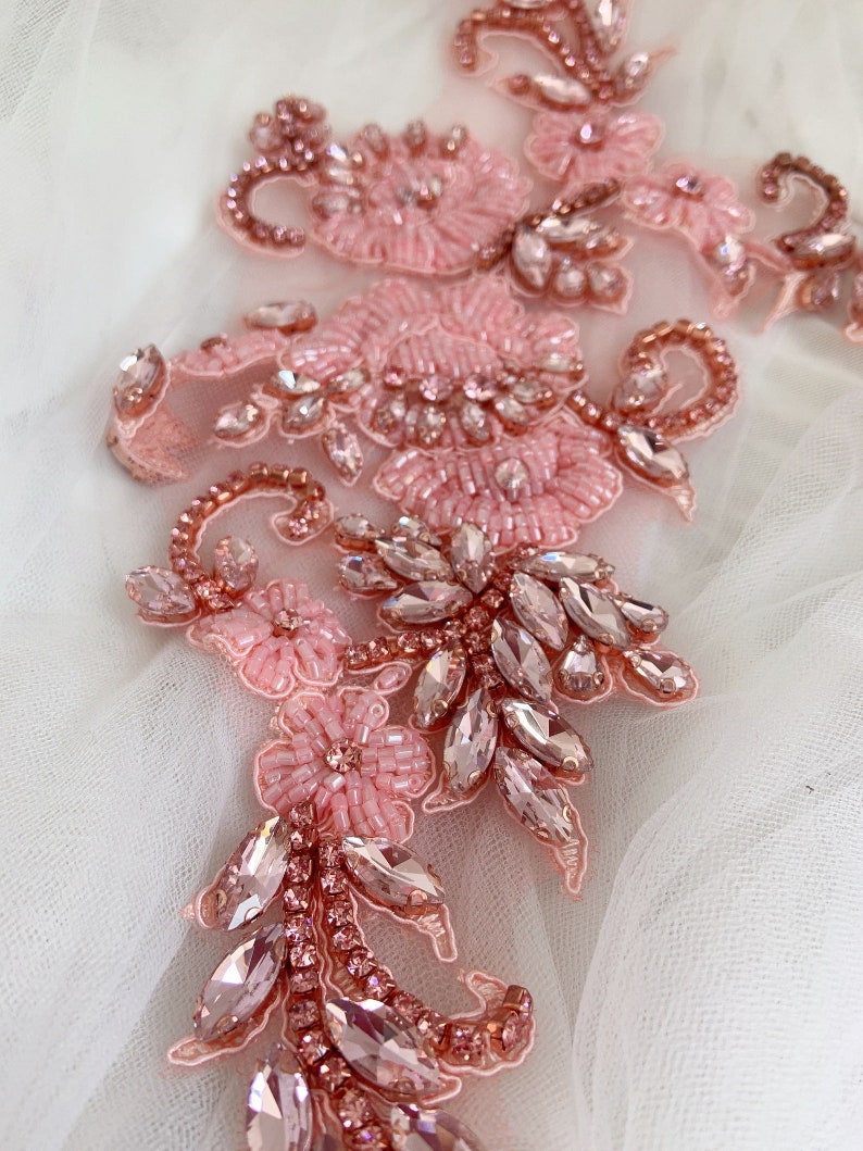 May include: Pink and rose gold beaded and rhinestone applique. The applique features a floral design with delicate beading and sparkling rhinestones.