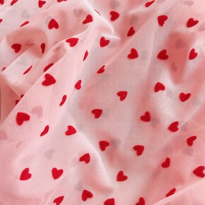 May include: Pink sheer fabric with a red heart pattern. The fabric is soft and delicate, and the hearts are evenly spaced.