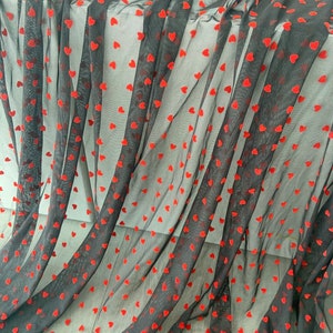 May include: Black sheer fabric with red velvet heart-shaped embellishments. The fabric is draped and folded, showing the texture of the hearts.