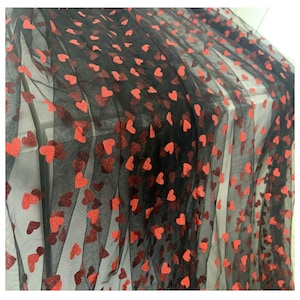 May include: Black tulle fabric featuring a pattern of red hearts. The hearts are of varying sizes and are spread across the sheer material. This fabric is suitable for clothing or decorative projects.