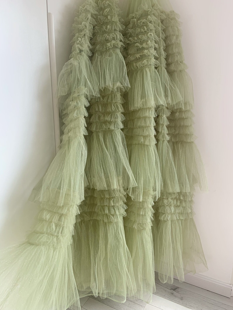 May include: A light green tulle skirt with multiple layers of ruffles. The skirt is made of a soft, delicate fabric and has a flowing, romantic look.