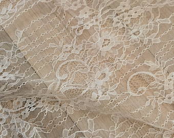 May include: White lace fabric with a delicate floral pattern. The lace is soft and sheer, and it has a slightly textured surface.