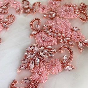May include: Pink and rose gold beaded and rhinestone floral applique. The applique features delicate flowers and leaves with sparkling rhinestones.