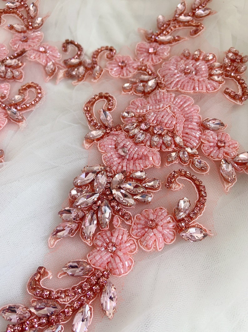 May include: Pink and rose gold beaded and rhinestone floral applique. The applique features delicate flowers and leaves with sparkling rhinestones.