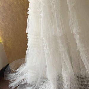 May include: A white tulle skirt with multiple layers of ruffles. The skirt is flowing and has a delicate, feminine look.