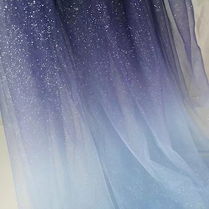 May include: A gradient tulle fabric with a blue to white ombre effect. The fabric is covered in small, silver glitter.
