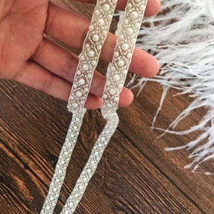 May include: Two white beaded trims with a geometric pattern. The trim is made of small white beads and a sheer fabric.