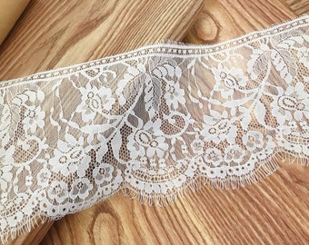 May include: White lace trim with a delicate floral pattern and a scalloped edge. The lace is approximately 1 inch wide.