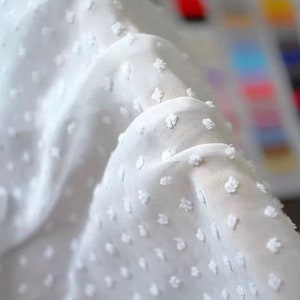 May include: White fabric with a small, raised dot pattern. The fabric is sheer and has a soft, delicate texture.