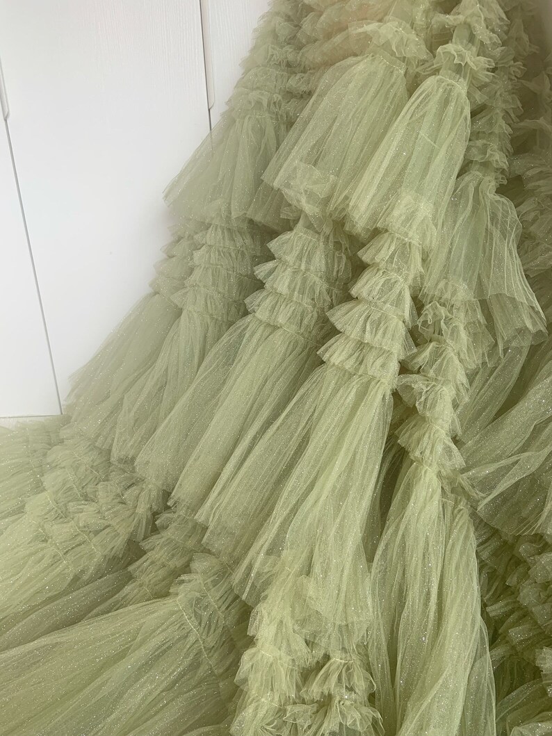May include: A green tulle fabric with a sparkly finish. The fabric is layered and ruffled, creating a voluminous and dramatic look.