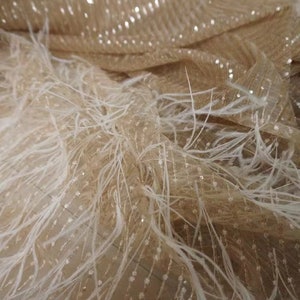 May include: Beige tulle fabric with white feather trim. The tulle has a subtle shimmer and the feathers are soft and delicate.