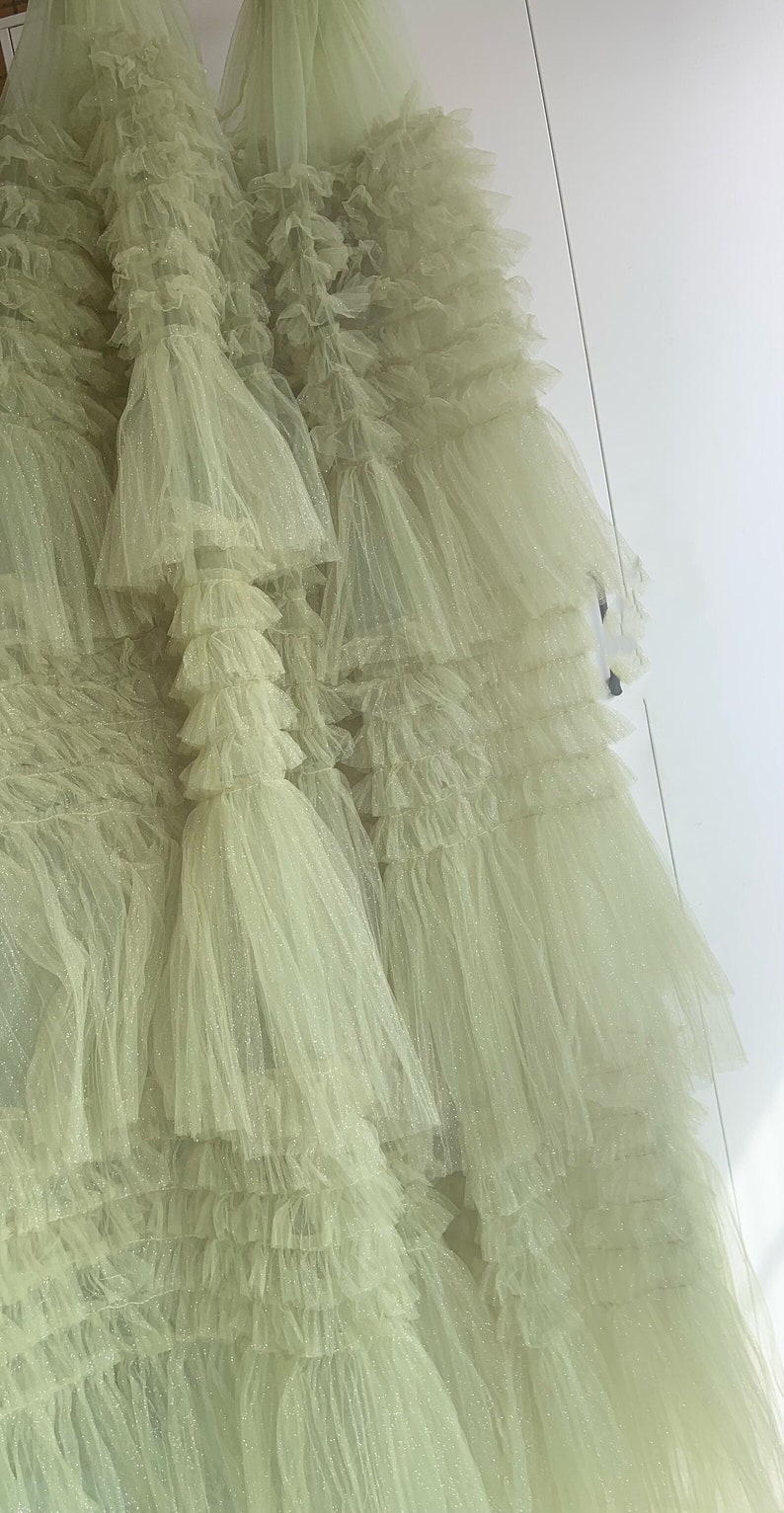 May include: A light green tulle skirt with multiple layers of ruffles. The skirt is made of a sheer fabric with a subtle sparkle.