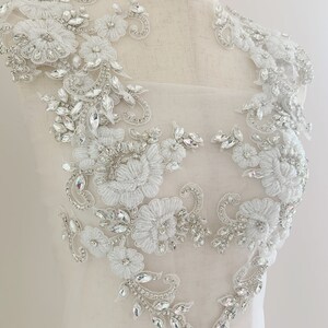 May include: White lace applique with crystal embellishments. The applique features floral designs and intricate details. This applique is perfect for adding a touch of elegance to any garment.