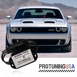 May include: A black electronic device with the text "POWER PACK QUICK CONNECT TURBO TUNER PROTUNINGUSA WWW.PROTUNINGUSA.COM" on it. The device is in front of a silver Dodge Challenger SRT.