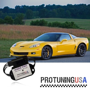 May include: A yellow Chevrolet Corvette sports car with a black roof and black wheels. The car is parked on a paved road with a green grassy field and trees in the background. A black electronic device with the text "POWER PACK QUICK CONNECT TURBO TUNER PROTUNINGUSA www.PROTUNINGUSA.com" is in the foreground.