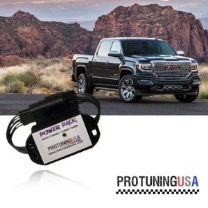 May include: A black power pack with the text "POWER PACK QUICK CONNECT TURBO TUNER" and "PROTUNINGUSA WWW.PROTUNINGUSA.COM" on it. The power pack is sitting on a white surface. The image also shows a black pickup truck in the background.