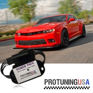 May include: A red Chevrolet Camaro sports car driving on a road. A black electronic device with the text "POWER PACK QUICK CONNECT TURBO TUNER PROTUNINGUSA WWW.PROTUNINGUSA.COM" is in the foreground.