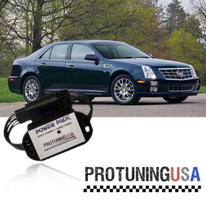 May include: A black power pack for a car with the text "POWER PACK QUICK CONNECT TURBO TUNER PROTUNINGUSA WWW.PROTUNINGUSA.COM" on it. The power pack is sitting on a black surface in front of a dark blue car.