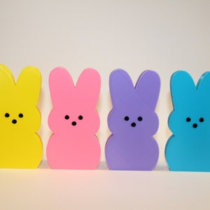 May include: Four pastel-colored bunny-shaped figures, yellow, pink, purple, and blue, standing in a row.