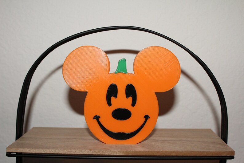 May include: Orange and black Halloween pumpkin shaped like Mickey Mouse with a green stem.