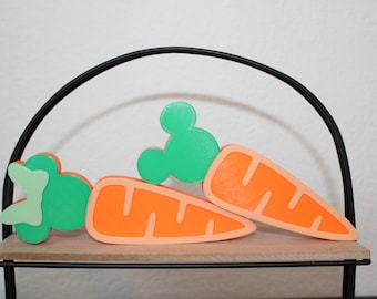 May include: Two orange and green carrot-shaped decorations with Mickey Mouse ears on a black metal shelf.
