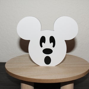 May include: White wooden Mickey Mouse head with black eyes, nose, and mouth. The head is sitting on a wooden stand.
