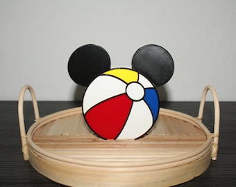 May include: A colorful beach ball design with black Mickey Mouse ears. The beach ball is red, white, yellow, and blue. The design is on a round, light brown tray with handles.