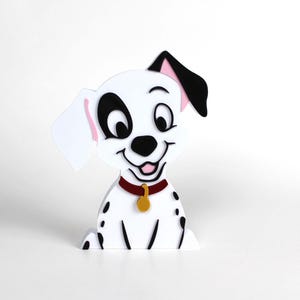 May include: A white and black Dalmatian puppy figurine with a red collar and gold tag. The puppy has black spots, a black ear, and a smiling face. The figurine is a decorative item.