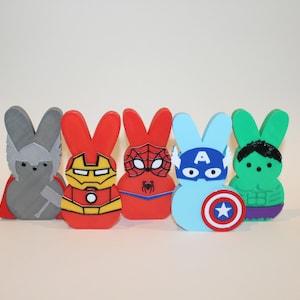 May include: Five Peeps candy bunnies decorated as superheroes. The bunnies are gray, red, red, blue, and green. The superheroes are Thor, Iron Man, Spiderman, Captain America, and the Hulk.
