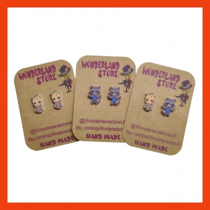 May include: Three cards with the text "WONDERLAND STORE" printed on them. Each card features a pair of handmade earrings with a cartoon image of a character from the Guardians of the Galaxy movie. The characters are Groot, Rocket Raccoon, and a second Rocket Raccoon. The cards also include the text "@Wonderlandstore" and "HAND MADE".