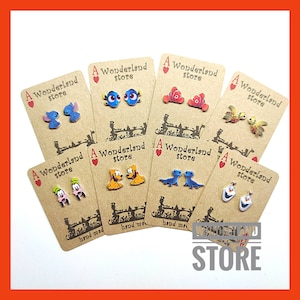 May include: A Wonderland Store card with a red heart and the text "A Wonderland Store" printed on it. The card features a pair of small, colourful, cartoon character earrings. The earrings are hand-made and feature characters from Disney movies, including Stitch, Dory, Nemo, Olaf, Mickey Mouse, and a pair of blue lizards.