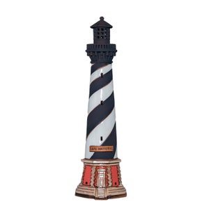 Op de afbeelding: Een keramische vuurtoren met zwart-witte spiraalstrepen. De bovenkant en de basis zijn donker, met een rode en bruine basis. De tekst "Cape Hatteras" staat op de zijkant. Een decoratief nautisch item.