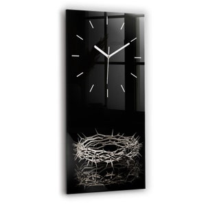 Può includere: Un orologio in vetro nero con quadrante e lancette bianche. L'orologio è posizionato su uno sfondo nero con una corona di spine argentata al centro inferiore dell'immagine.