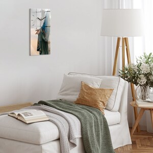 Puede incluir: Un sofá blanco con una manta verde y una almohada de color beige. Una lámpara blanca con un trípode de madera está en el fondo. Una pequeña mesa de madera con un jarrón de flores blancas está en la esquina.