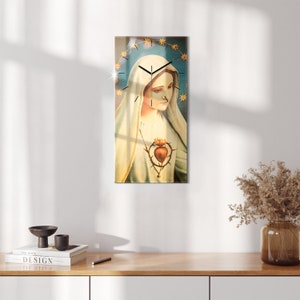 Puede incluir: Un reloj de vidrio con una imagen vintage de la Virgen María. La esfera del reloj está rodeada por un halo de estrellas doradas. La Virgen María lleva una túnica blanca y una capa azul. Tiene una corona de espinas y un corazón con una espada que lo atraviesa.