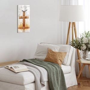 Puede incluir: Un sofá blanco con una manta de lana verde y una almohada marrón. Un reloj con un diseño de cruz de madera está colgado en la pared detrás del sofá.